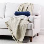 Natural and navy woven throws styled together on a cream sofa, featuring textured finishes and fringed edges.