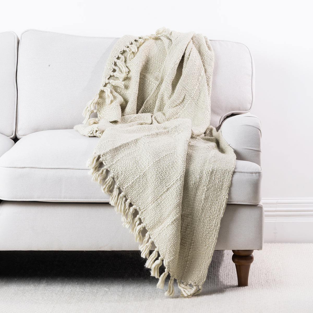 Natural woven throw draped over a cream sofa, featuring a textured finish and fringed edges.