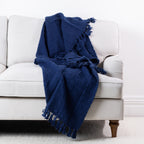 Navy woven throw draped over a cream sofa, featuring a textured finish and fringed edges.