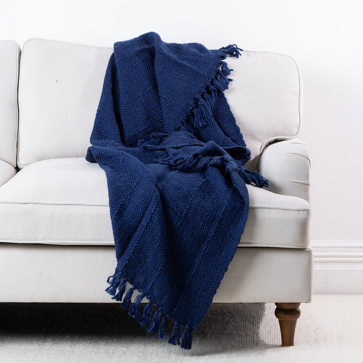 Navy woven throw draped over a cream sofa, featuring a textured finish and fringed edges.