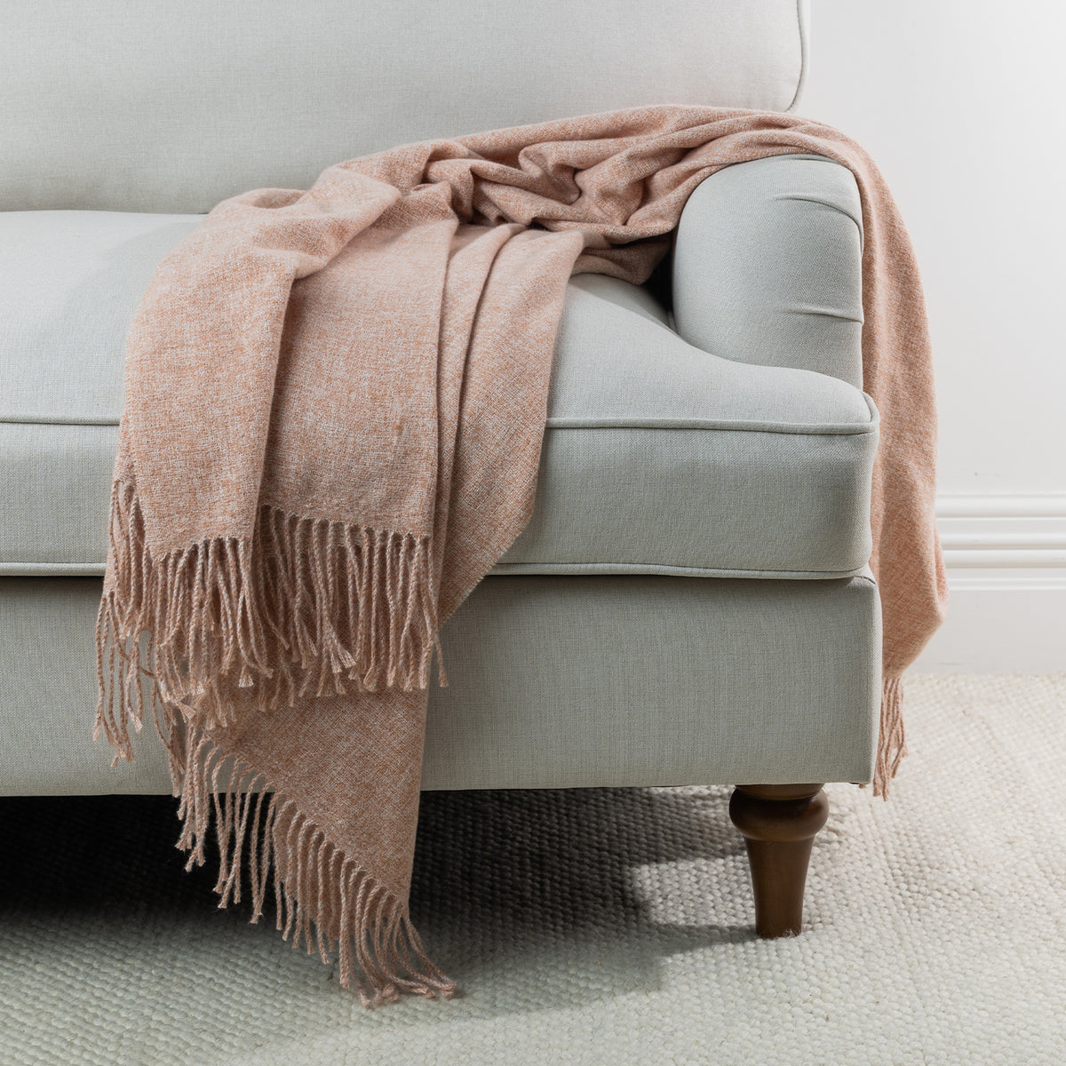 Rust: Solace Simone Throw in rust draped over the arm of a light grey sofa, featuring a soft woven texture and fringed edges.
