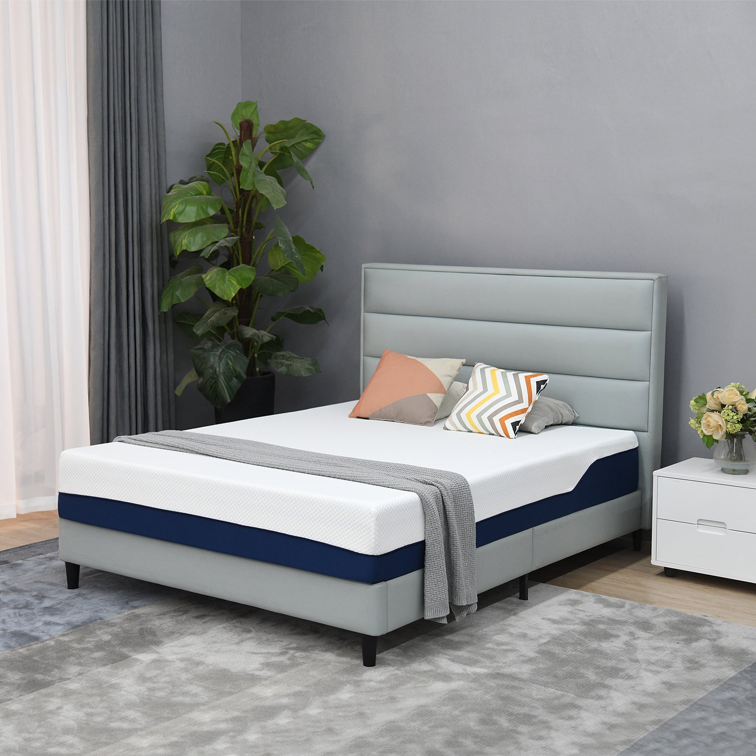 Modern bedroom scene featuring a light grey upholstered bed with a white and navy mattress, styled with neutral cushions, a grey throw, and contemporary décor.
