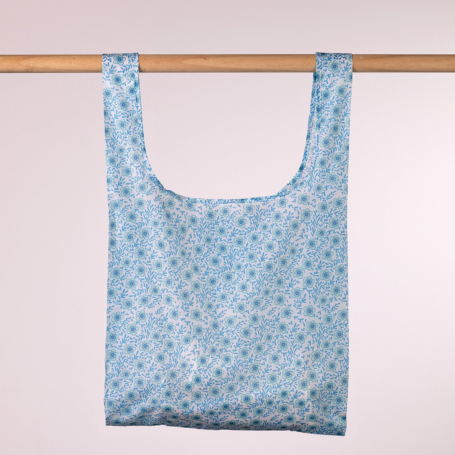 Reusable shopping bag with blue floral pattern hanging on a wooden rod against a white background