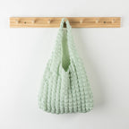 Green woven bag hanging on a wooden rack against a white wall