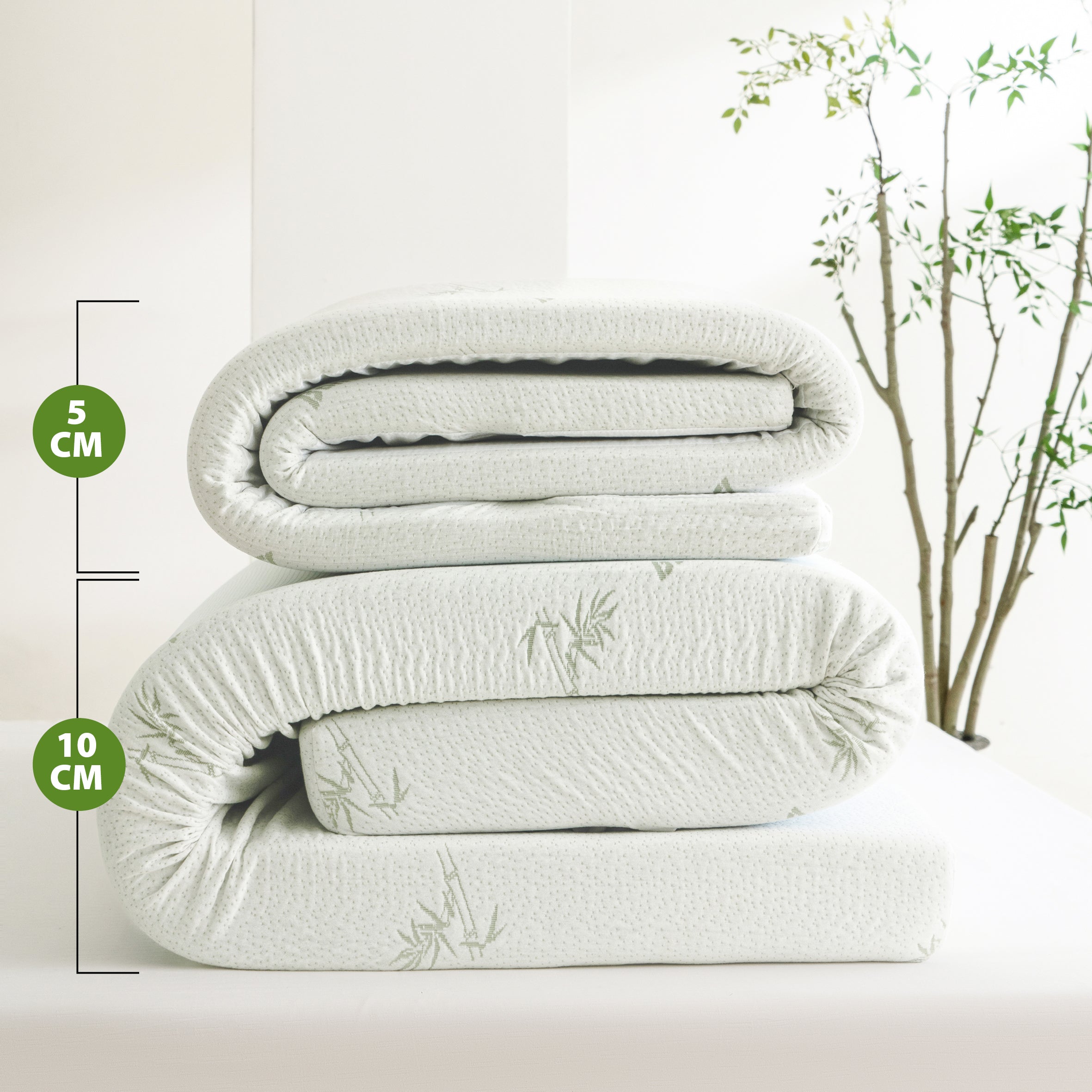 Comparison of Bambou Memory Foam Mattress Toppers showing 5cm and 10cm depth options folded on a bed, highlighting the difference in thickness and bamboo-patterned cover.