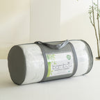 Bambou 10cm Memory Foam Mattress Topper rolled and packed in a clear carry bag with grey handles, displayed on a tabletop in a bright bedroom setting.