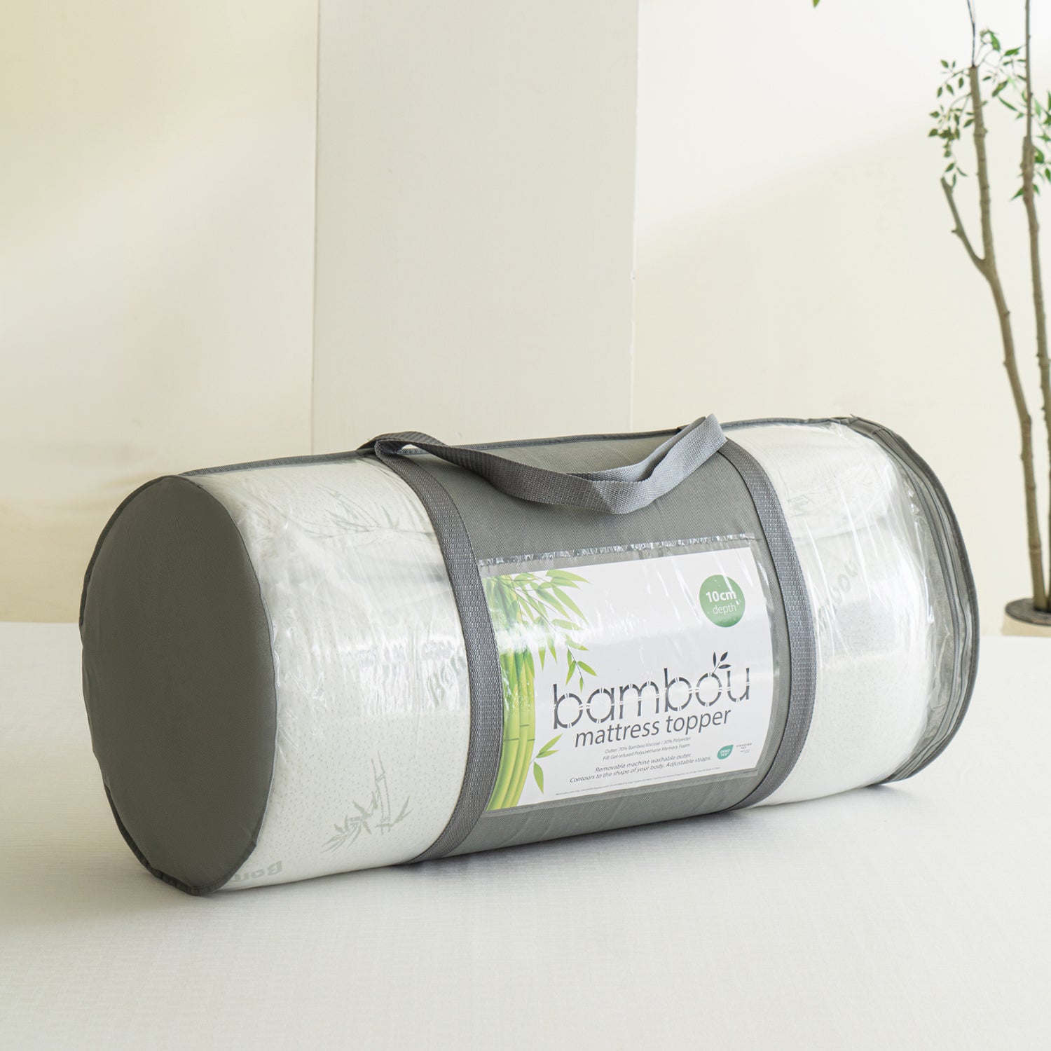 Bambou 10cm Memory Foam Mattress Topper rolled and packed in a clear carry bag with grey handles, displayed on a tabletop in a bright bedroom setting.