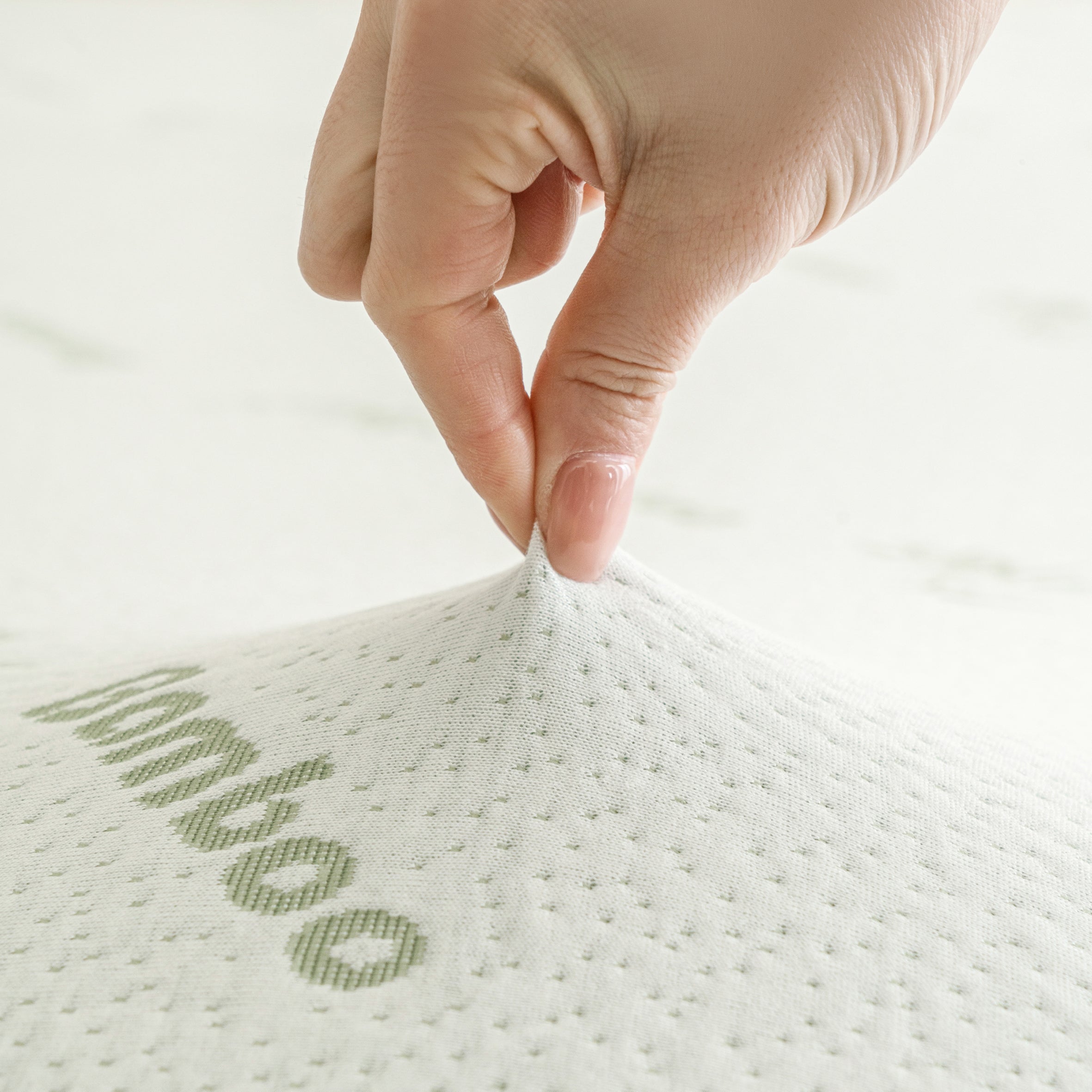 Close-up of a hand pinching the bamboo-blend cover of the Bambou Memory Foam Mattress Topper, highlighting the soft textured fabric and bamboo-patterned design.