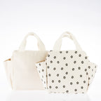 Two cream corduroy lunch totes, one plain and one with a brown daisy print, featuring carry handles and side pockets.