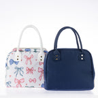 Two lunch totes with zip closures and carry handles, one featuring a colourful bow print and one in plain navy.