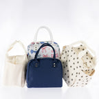 Assorted lunch totes in cream corduroy, navy, colourful bow print, and brown daisy print with carry handles on a white background.