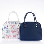 Two lunch totes with zip closures and carry handles, one featuring a colourful bow print and one in plain navy.