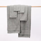 Design Plus Tia Plush 600gsm Towel Pack in silver displayed over a wooden rail.