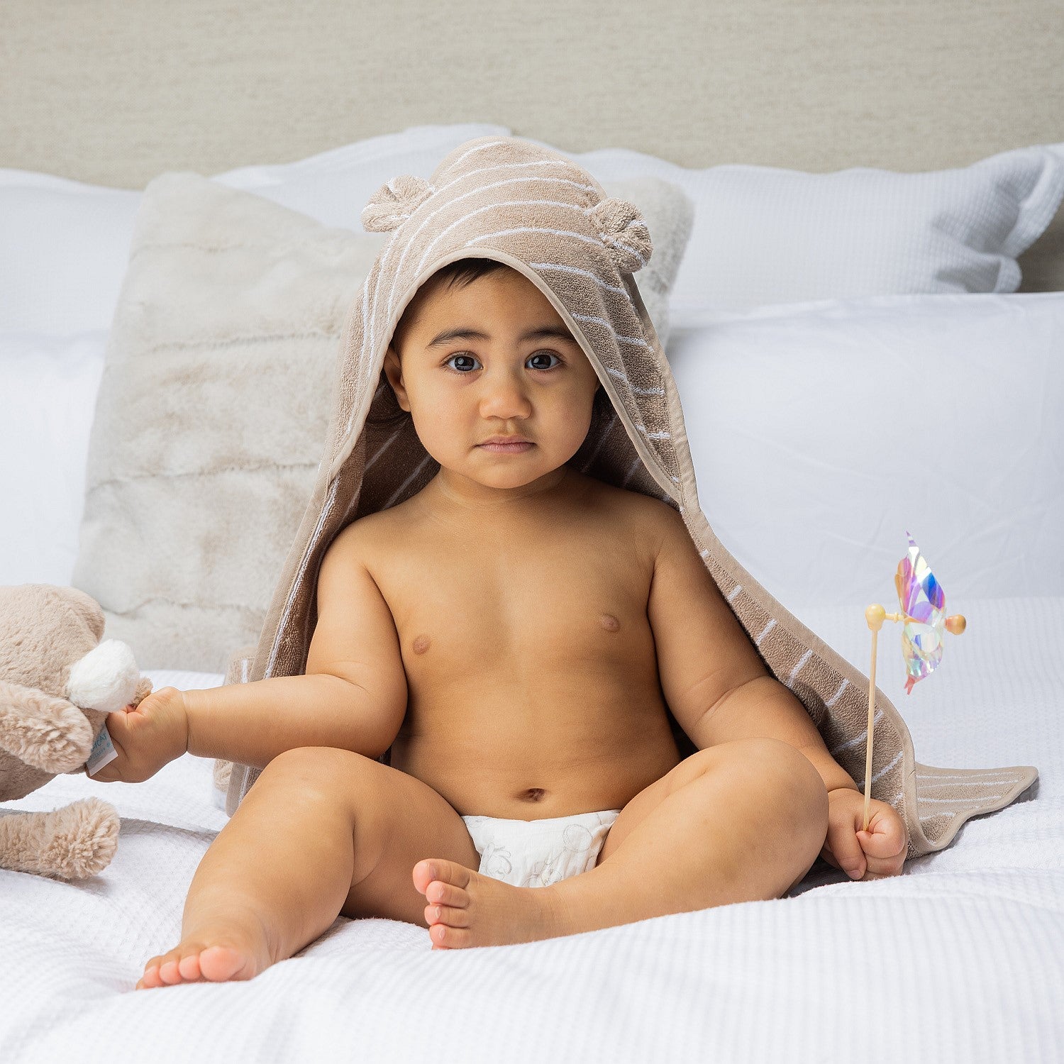 Baby sitting on a bed wearing a hooded towel with bear ears.