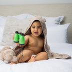 Baby sitting on a bed wearing a hooded towel with bear ears.