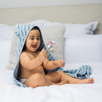 Baby sitting on a bed wearing a hooded towel with bear ears.