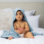 Baby sitting on a bed wearing a hooded towel with bear ears.