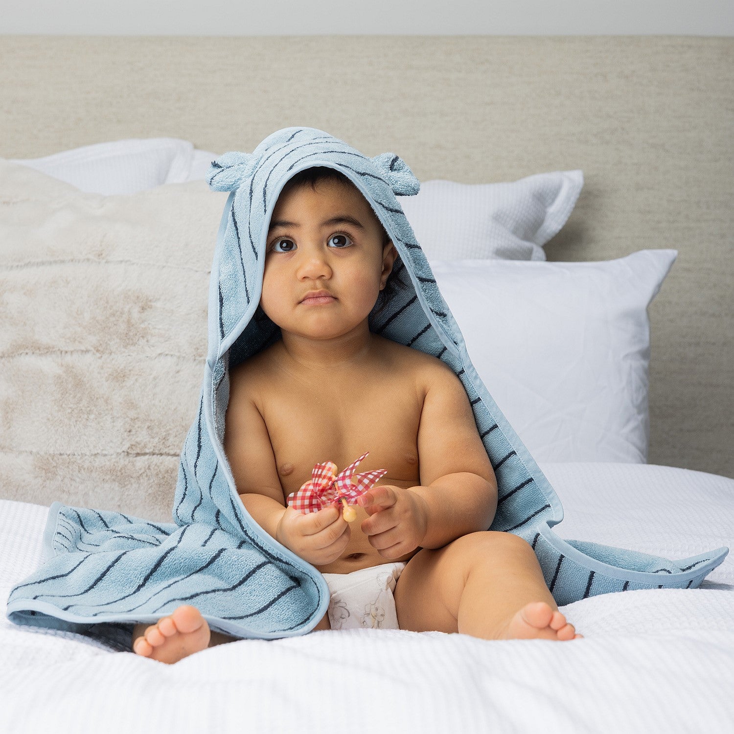 Baby sitting on a bed wearing a hooded towel with bear ears.