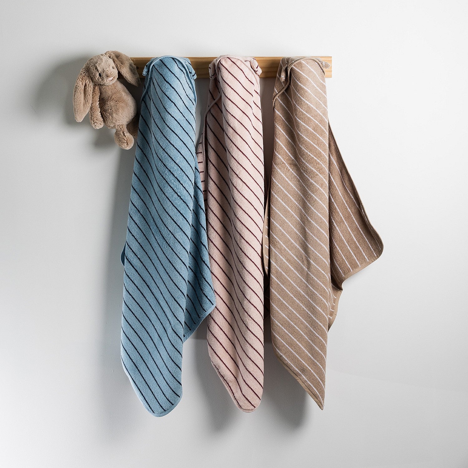 Three bath hooded towels in blue, pink, and natural hanging side by side.