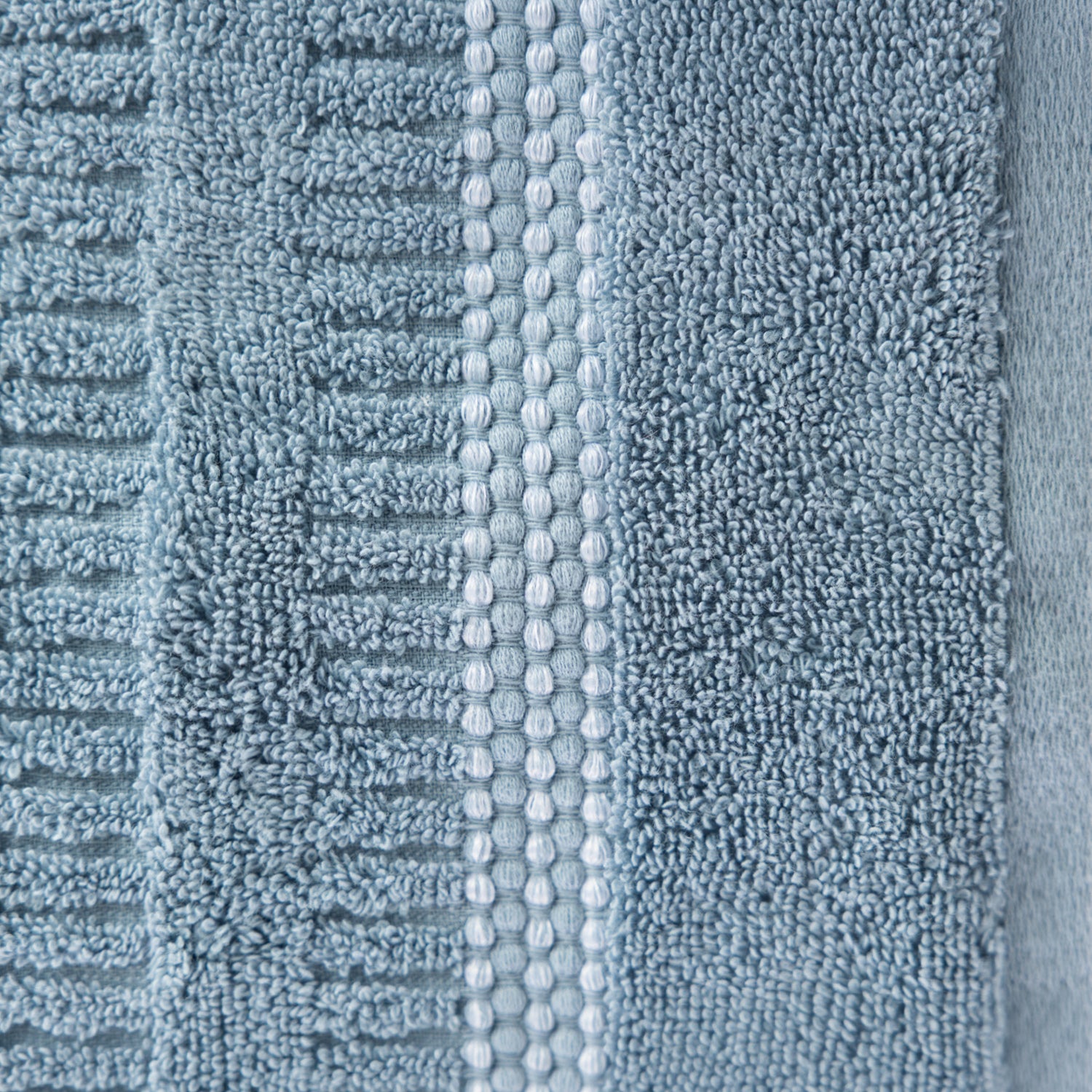 Close-up of the Home Co. Penny Self Stripe Face Cloth in dusty blue, showing the soft textured cotton loops, raised stripe pattern and decorative border detail.