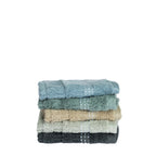 Stack of Home Co. Penny Self Stripe face cloth in blue, seafoam, natural, pale green and charcoal, showing the textured stripe design and decorative border detail.