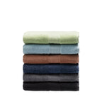 Stack of six folded plush bath towels in French pear, sky blue, brick, navy, smoke and black.
