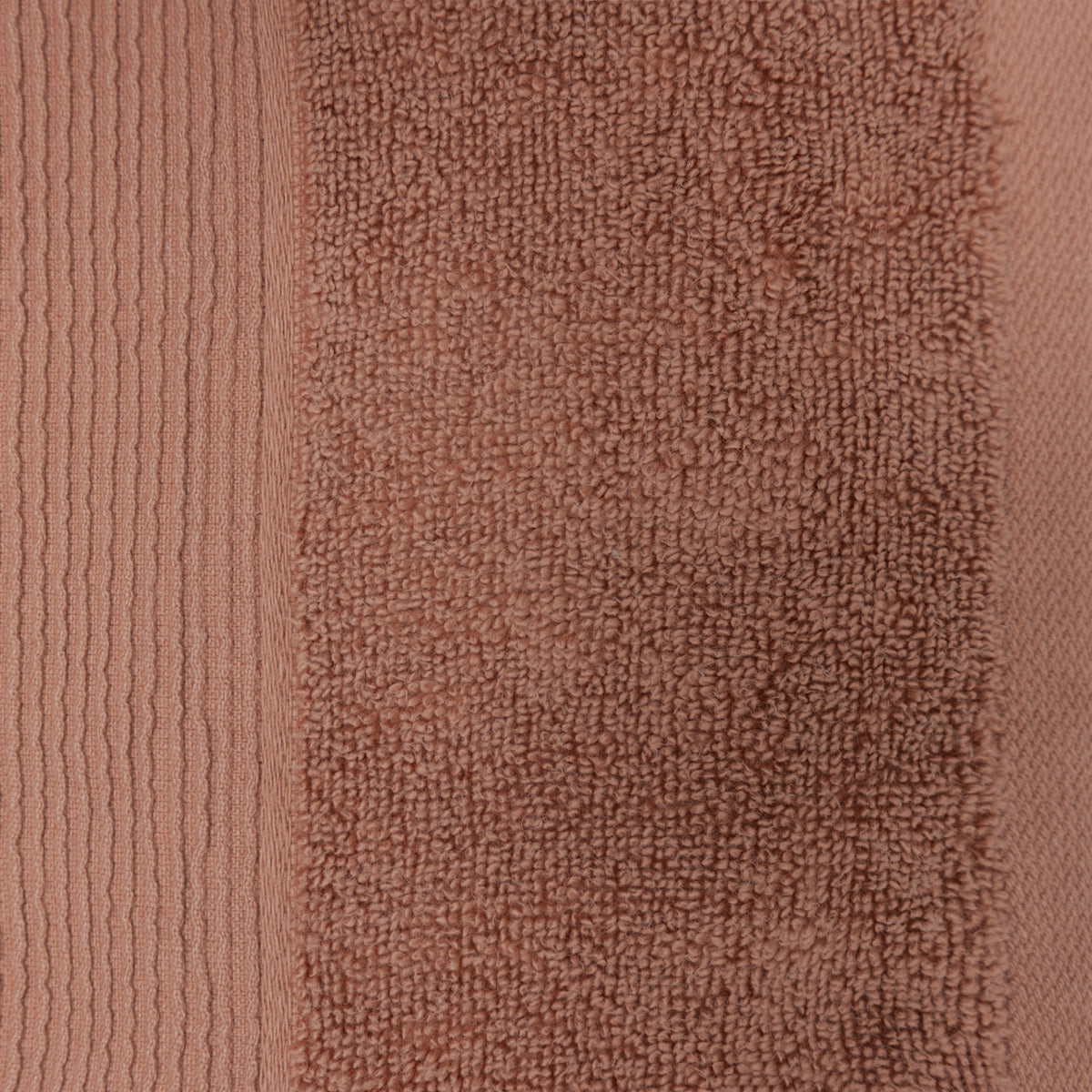 Close-up of a brick-coloured plush bath towel showing the textured cotton pile and ribbed border detailing.
