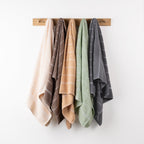 Home Co. Sara Stitch towel range hanging from a wooden wall rack in cream, mocha, peach, sage green and charcoal, showcasing the coordinating stitched stripe design.