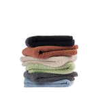 A stack of folded Home Co. Nevada Hand Towels featuring a soft textured surface in black, rust, beige, sage green, charcoal and pale blue, displayed against a white background.