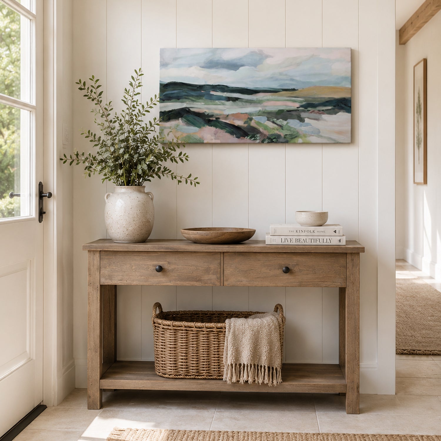 A serene modern country hallway is styled with an abstract landscape canvas above a rustic timber console table, complemented by natural textures, greenery, and soft neutral décor.