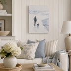 A soft coastal artwork depicting a person and their dog strolling along a tranquil shoreline, beautifully styled in a light, modern country living room with blue and neutral accents.