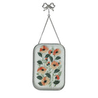 Silver framed glass wall art with orange floral artwork and bow hanging hook on a white background.