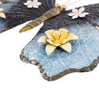 Close-up of the blue butterfly wall hanging showing the textured metal wing and raised yellow flower detail.