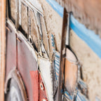 Close-up of a textured metal wall art piece depicting stylized vintage cars in red, cream, blue, and brown tones.