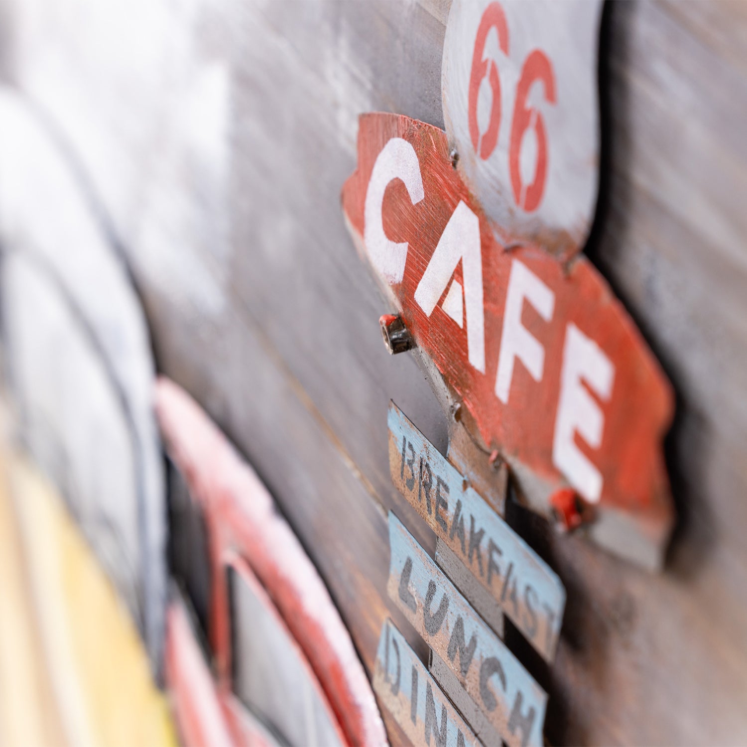 A close-up of a rustic wall art featuring a red '66 CAFE' sign, with layered stencil-style text elements for 'Breakfast', 'Lunch', and 'Dinner' in multi tones.
