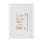 A framed wall art print with the phrase 'Rain down the good vibes.' in soft tan lettering, accompanied by a simple showerhead illustration.