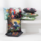 A collection of outdoor cushions with various colorful tropical and nature prints, arranged on and beside a white wooden bench against a white wall.
