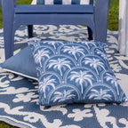 A blue & white palm design outdoor cushion arranged in an outdoor setting.