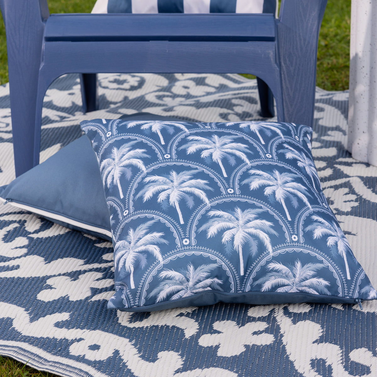 A blue & white palm design outdoor cushion arranged in an outdoor setting.