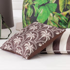 A mocha & white palm design outdoor cushion arranged with outdoor accessories.