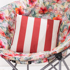 An outdoor cushion with vertical red and white stripes sits on a tropical floral moon chair with gray metal legs.