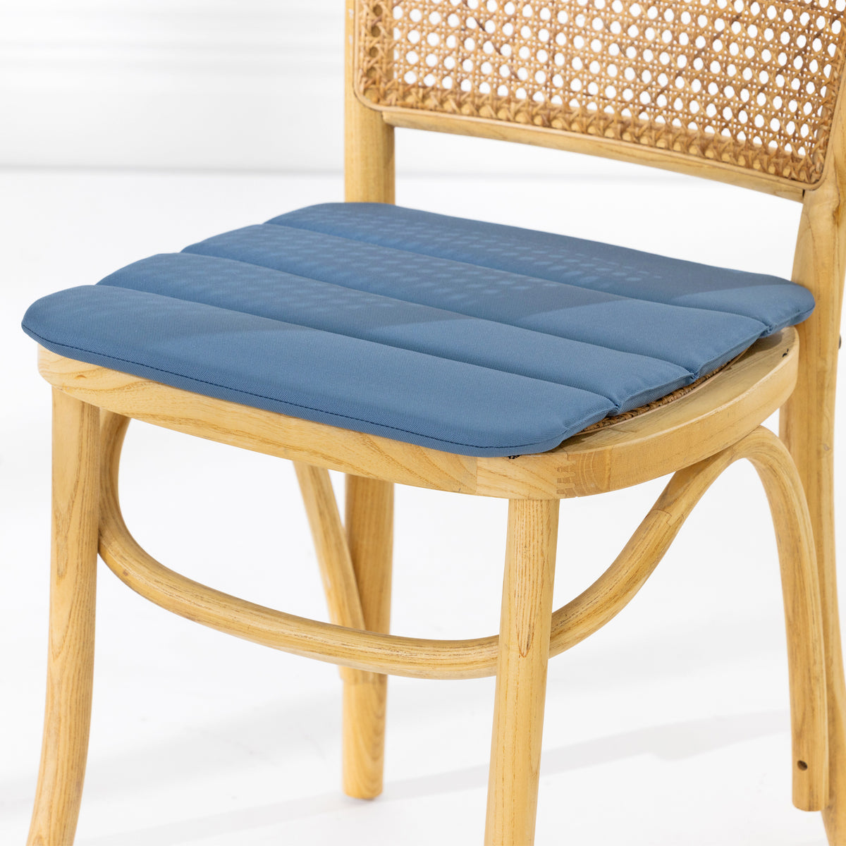 A dining chair with a natural woven cane backrest and a padded blue seat cushion, shown against a clean white studio background.