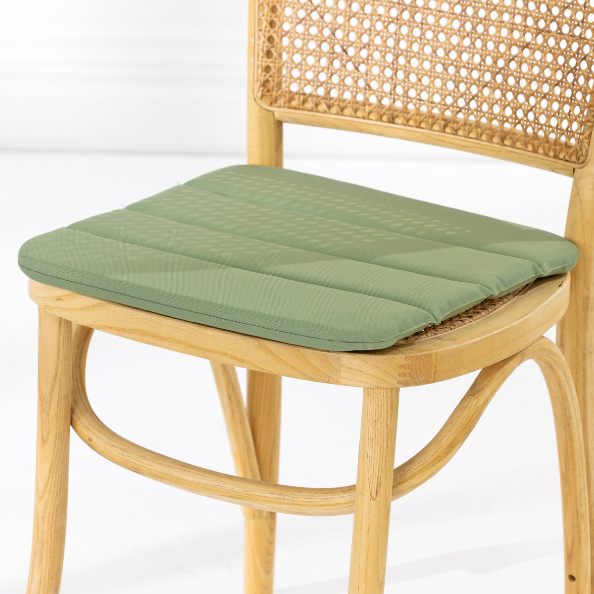 A dining chair with a natural woven cane backrest and a padded green seat cushion, shown against a clean white studio background.