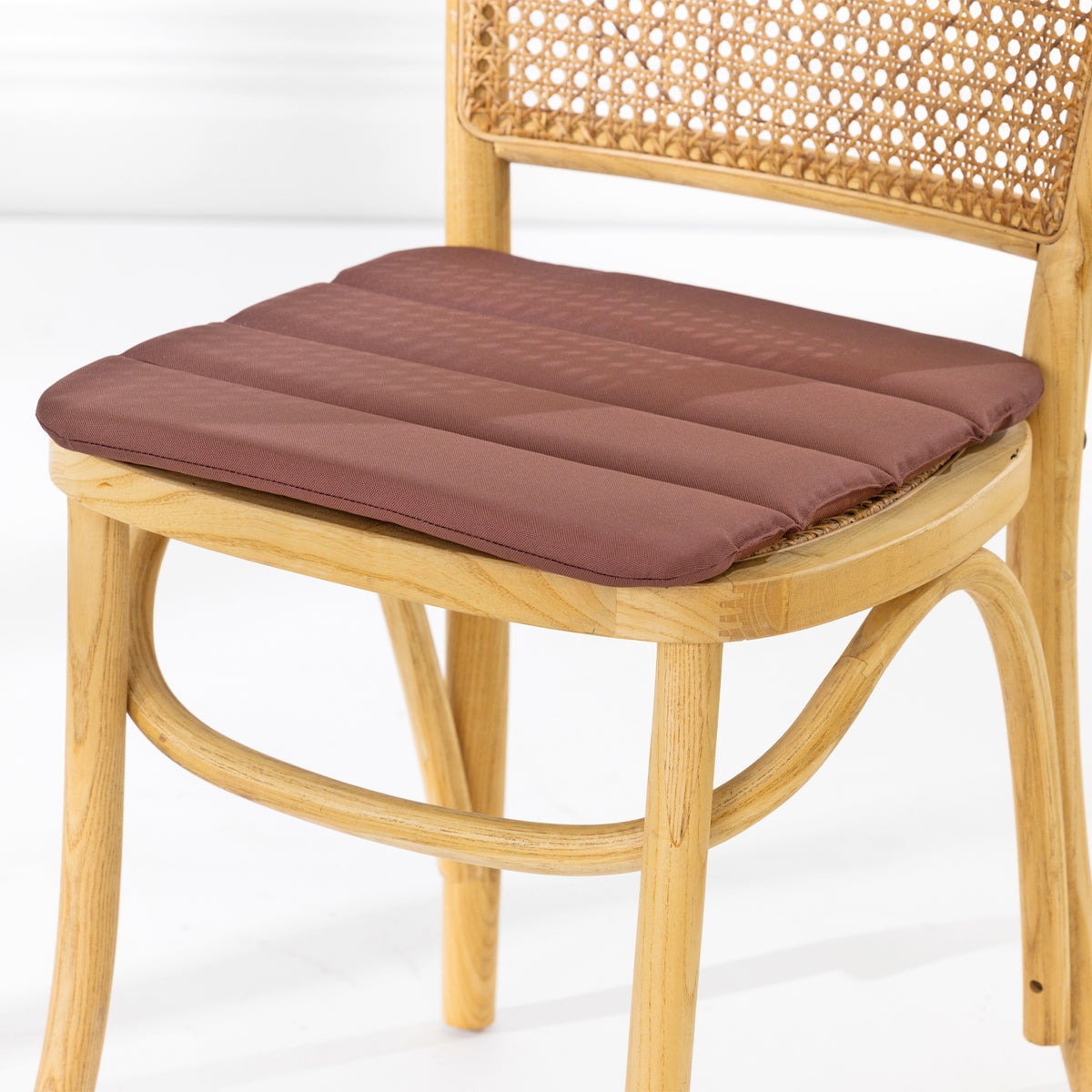 A dining chair with a natural woven cane backrest and a padded mocha seat cushion, shown against a clean white studio background.