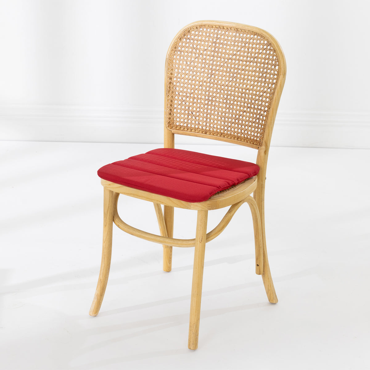 A dining chair with a natural woven cane backrest and a padded red seat cushion, shown against a clean white studio background.