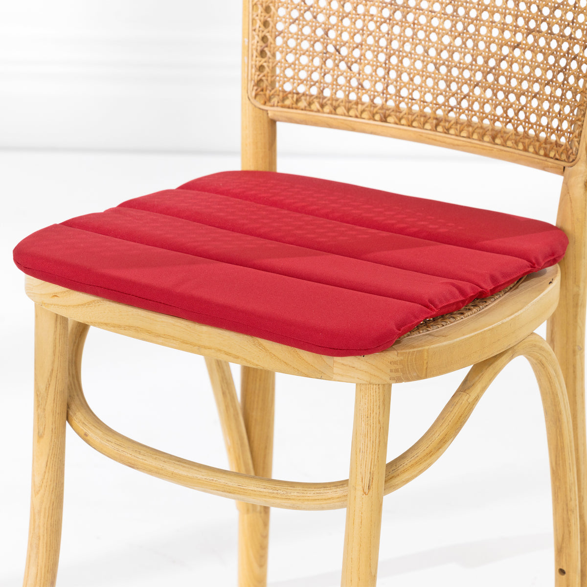 A dining chair with a natural woven cane backrest and a padded red seat cushion, shown against a clean white studio background.
