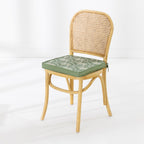 A light natural wood dining chair with a woven cane backrest and a green cushioned seat featuring a white palm pattern, set against a clean white background.