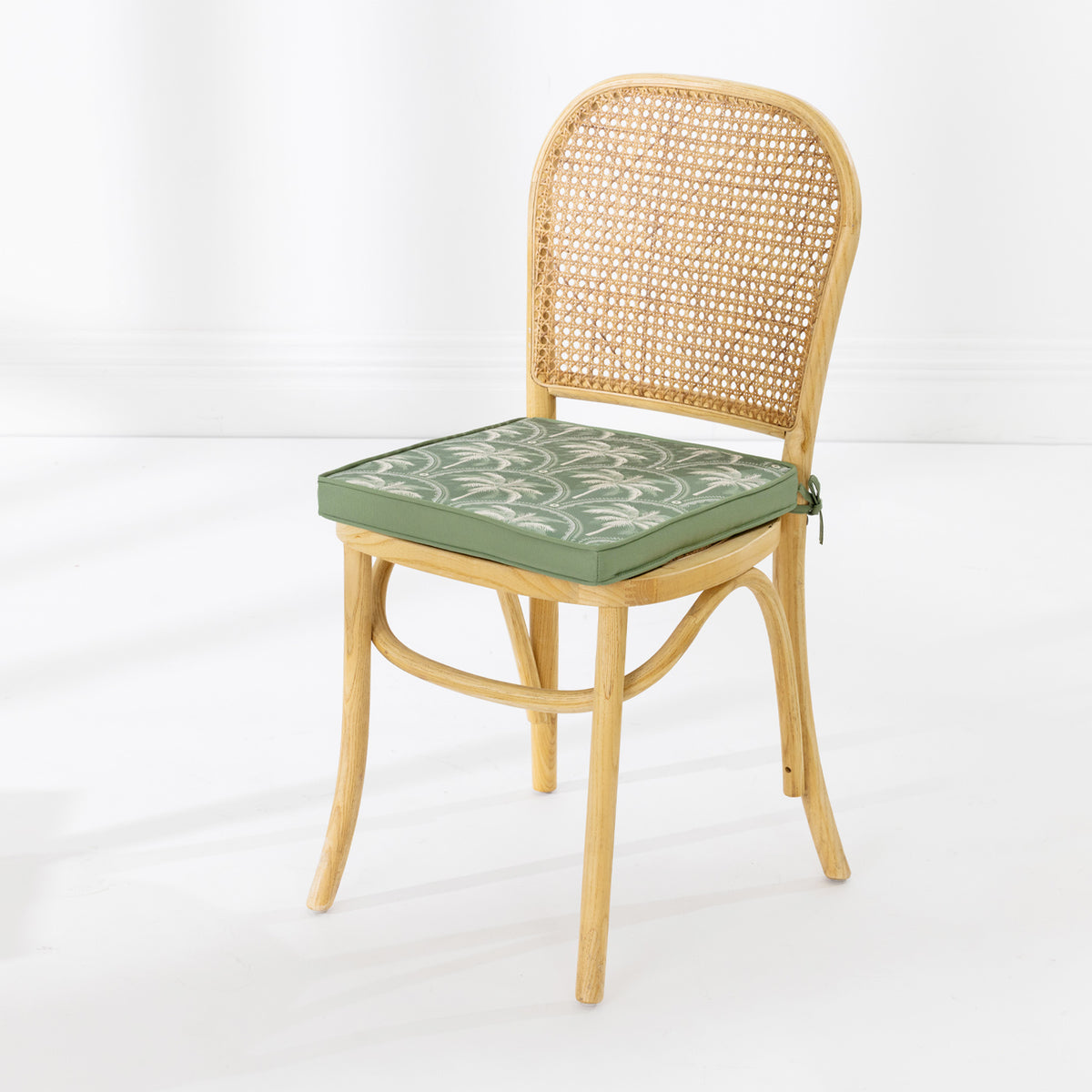 A light natural wood dining chair with a woven cane backrest and a green cushioned seat featuring a white palm pattern, set against a clean white background.
