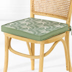 A light natural wood dining chair with a woven cane backrest and a green cushioned seat featuring a white palm pattern, set against a clean white background.