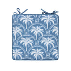 A outdoor chair pad with a white palm tree and scalloped arch pattern, finished with two matching blue tie straps at the top corners, shown on a plain white background.